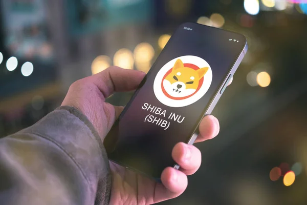 SHIBA INU şifreleme sembolü, logo. İş ve finansal konsept. Akıllı telefon ile el, kripto simgesi ile ekran kapatma