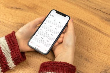 Kharkov, Ukrayna - 17 Kasım 2021: Kadın Takvim 2022 uygulamasını Apple iPhone ekranında aç. Ahşap arkaplan 