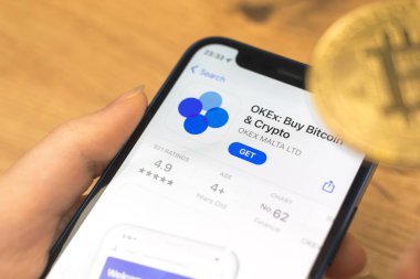Kharkov, Ukraine - January 10, 2022: OKEx Buy Bitcoin Crypto app icon close-up. Woman with application on Apple iPhone 12