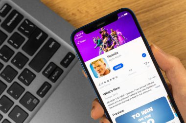 Kharkov, Ukrayna - 14 Ocak 2022: Fornite oyunu için Apple iPhone kullanıyor. Tahta masadaki dizüstü bilgisayar, iş geçmişi.