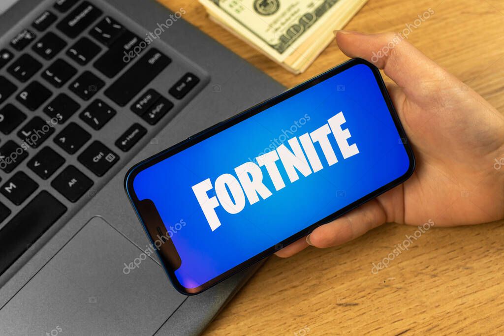 Kharkov, Ukraine - January 14, 2022: Mobile phone with Fortnite logo. Laptop on wooden table, business background