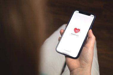 Kharkov, Ukrayna - 10 Ocak 2022: Kadın Heartify uygulaması kullanıyor. Apple iPhone 12 ile el, logolu cep telefonu ekranı