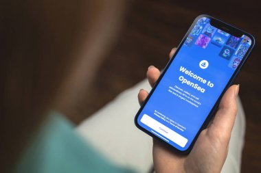Kharkov, Ukrayna - 10 Ocak 2022: Kadın OpenSea NFT uygulaması kullanıyor. Apple iPhone ile el, logolu cep telefonu ekranı