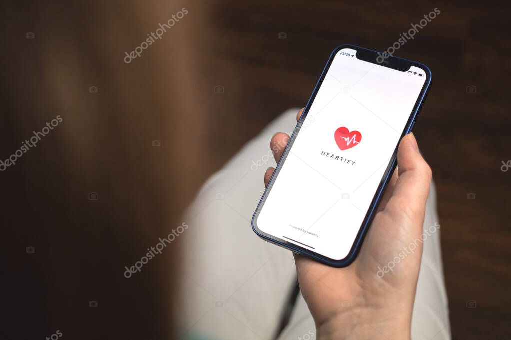 Kharkov, Ukraine - January 10, 2022: Woman uses Heartify app. Hand with Apple iPhone 12, mobile phone screen with logo
