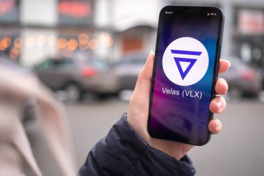 Kharkov, Ukrayna - 2 Şubat 2022: Velas VLX madeni para sembolü. Şifreli para ticareti, dijital ve sanal para, mobil bankacılık. Akıllı telefon ile el, kripto simgesi ile ekran yakın çekim