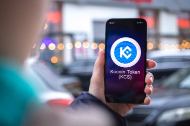 Kharkov, Ukrayna - 2 Şubat 2022: Kucoin KCS sembol. Şifreli para ticareti, mobil bankacılık. Akıllı telefon ile el, kripto simgesi ile ekran yakın çekim