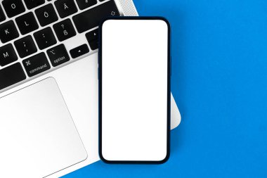 Üst görünüm modeli. Beyaz ekranlı akıllı telefon, dizüstü bilgisayarlı düz mavi arka plan. Asgari çalışma alanı, modern dizüstü bilgisayar, kopyalama alanı 