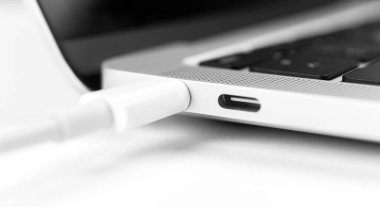 Pil dizüstü bilgisayarı yükleniyor. Hızlı şarj için modern USB C portu. Dizüstü bilgisayara takılı beyaz kablo yakın çekim görüntüsü