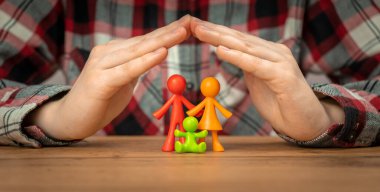 Genç aile sigortası konsepti. Elleri ahşap bir masanın üzerinde renkli aile figürleri ile kaplı. Güvenlik ve destek