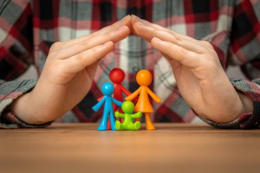 Aile sigortası konsepti. Elleri ahşap bir masanın üzerinde olan renkli aile figürleri. Güvenlik ve destek