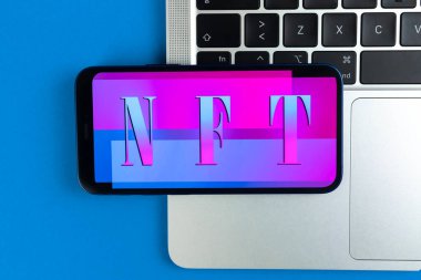 NFT karşılanamaz marka arkaplan. Modern engelleme teknolojisi, kripto sanatı ve kripto para biriminin geleceği. Laptop klavyesinde cep telefonu, üst görünüm 