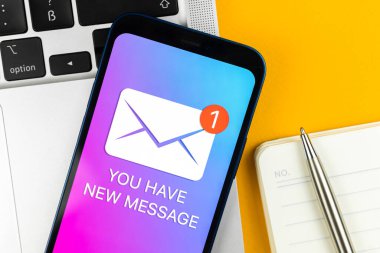 Cep telefonunun yakın çekim görüntüsünde yeni bir mesaj bildiriminiz var. İş iletişimi konsepti, dizüstü bilgisayar ve ofis masası geçmişi