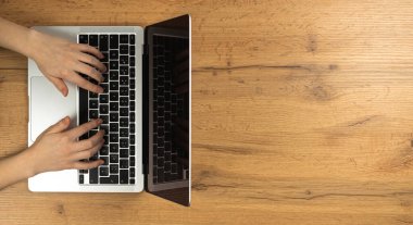 Ahşap bir arka planda kadın elleri ve dizüstü bilgisayarı. Çalışma alanı kavramı, evde çalışmak, bilgisayar ve serbest çalışmak, tasarım. Düz konum, üst görünüm ve boşluk kopyala