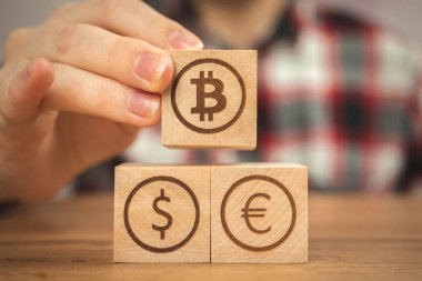 Bitcoin, dolar ve avro sembolleri ellerinde tahta küplerin üzerinde. Kripto para ve nakit geçmişi kavramı, ahşap masa.