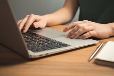 Laptop ahşap masada ve genç kadın eli klavyede. Serbest iş yeri, ev kavramından çalışma