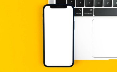 Apple iPhone model ekran, dizüstü bilgisayarlı düz masa, sarı arka plan. Asgari tasarım, cep telefonu modeli, üst görünüm, kopyalama alanı 