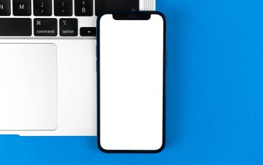 Apple iPhone model ekran, dizüstü bilgisayarlı düz masa, mavi arka plan. Asgari tasarım, cep telefonu modeli, üst görünüm, kopyalama alanı 