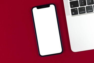 Apple iPhone maketi, dizüstü bilgisayarlı ofis masaüstü, kırmızı bordo arka plan. Üst görünüm, uzay fotoğrafını kopyala