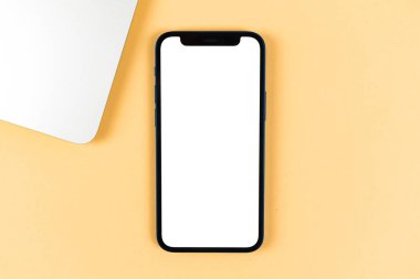 Apple iPhone maketi düz yatıyordu, bilgisayarlı ofis masaüstü, parlak bej arka plan. Üst görünüm, uzay fotoğrafını kopyala