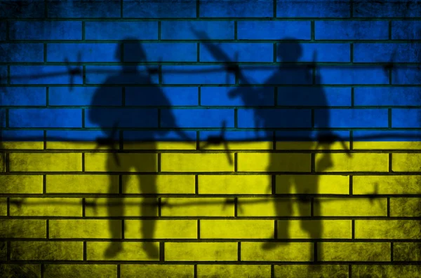 Прапор України та військове минуле. Колючий паркан і озброєний силует. Конфлікт і військова концепція. Текстура гранджу на цегляній стіні. — стокове фото