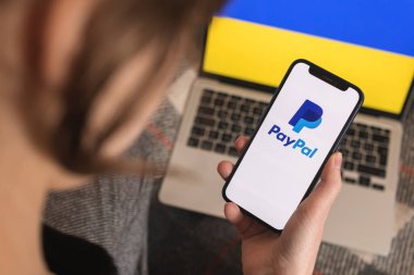 Kharkov, Ukrayna - 18 Mart 2022: Ukrayna 'da Paypal kullanan genç kadın. Arkaplanda logo ve Ukrayna bayrağı olan cep telefonu