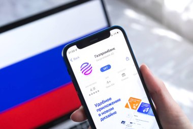 SPB, Rusya - 7 Nisan 2022: Rusya 'da Gazprombank mobil bankacılık uygulaması. Akıllı telefonlu el, ekranda ikon. Ulusal bayrak fotoğraflı arkaplan