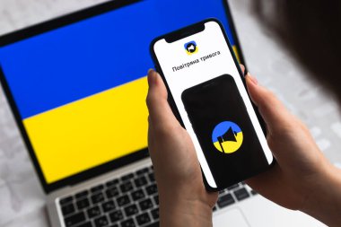 Poltava, Ukrayna - 8 Nisan 2022: Kadın cep telefonu için Air Raid Siren uygulaması kullanıyor. Ukrayna için modern hava alarmı uygulamalı akıllı telefon. Arkaplanda bayrak 