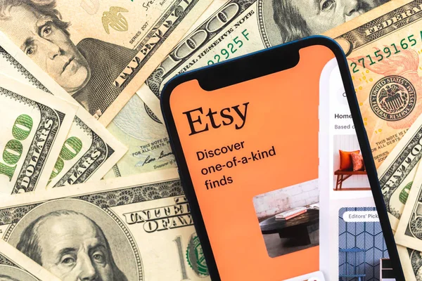 Poltava, Ukrayna - 28 Nisan 2022: Cep telefonu ekranında Etsy alışveriş uygulaması logosu. Dolar para banknotları ile iş geçmişi 