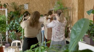 Sanat dersine katılan bir grup kadın. Bayan öğrenciler ve öğretmen birlikte atölyede Boho stilinde ev dekorasyonu yapıyorlar. Sanat okulu stüdyosunda el yapımı makrome örüyor. Yaratıcılık, insanların eğitimi