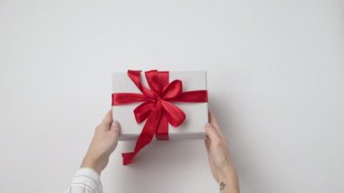 Kadın, beyaz arka planda kırmızı fiyonk olan boş el sanatları hediye kutusunu açıyor. Noel, yeni yıl, doğum günü, tatil, yıldönümü konsepti. Üst manzara, düz uzanma.