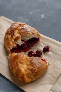 Bakery pastries on grey background. Freshly cooked bakery with cherry for delivery or take away. Home cooked bakery for morning breakfast. Copy space. Vertical shot. Selective focus
