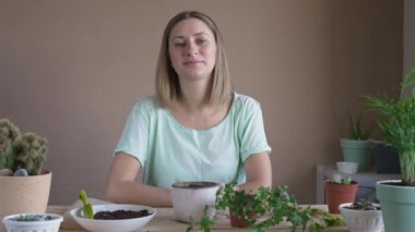Portrait of smiling girl planting a flower in a pot. Woman transplanting indoor plants, growing and grooming home flowers. Plants care concept. Home Garden.