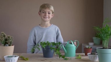 Portrait of smiling boy planting and watering a flower in a pot. Child transplanting indoor plants, growing and grooming home flowers. Plants care concept. Home Garden.