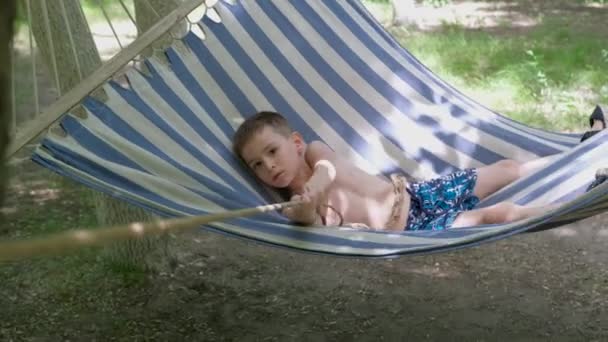 夏のアウトドアを楽しむ小さな男の子 キャンプでハンモックに寝そべっている子供 子供時代 自由の概念 — ストック動画