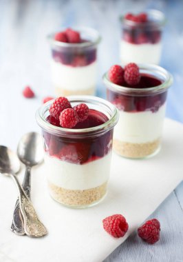 Ahududu krem peynirli tatlı ve mavi arka planda bir bardakta servis edilen kurabiye tabanı..