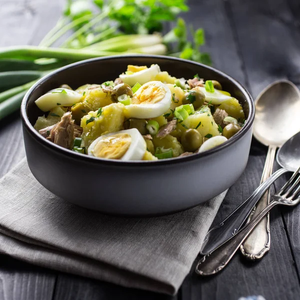 Akdeniz Patates Salatası, yumurta, ton balığı ve zeytinli, siyah ahşap arka planda bir kasede servis edilir..
