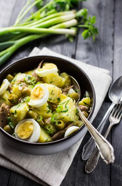 Akdeniz Patates Salatası, yumurta, ton balığı ve zeytinli, siyah ahşap arka planda bir kasede servis edilir..