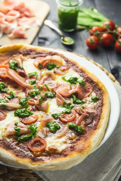 Prosciutto ve pesto pizzası. Koyu ahşap arka planda kiraz domatesli..