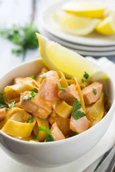 Limon dilimi ve maydanozlu garnitürle servis edilen beyaz bir kasede İtalyan somonu ve limonlu tagliatelle makarna.