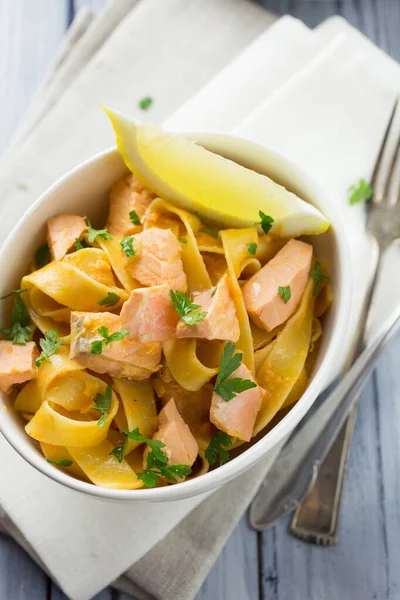Limon dilimi ve maydanozlu garnitürle servis edilen beyaz bir kasede İtalyan somonu ve limonlu tagliatelle makarna.