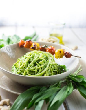 Bir kase dolusu yeşil pesto spagettisi ve hafif bir tabakta ızgara domates.