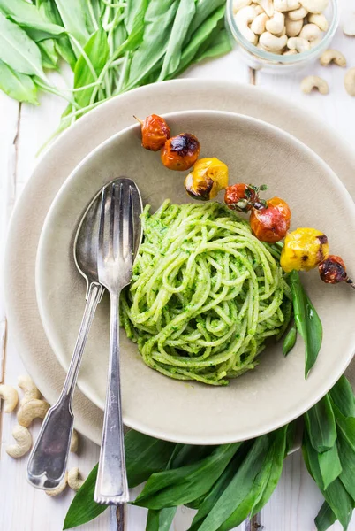 Bir kase dolusu yeşil pesto spagettisi ve hafif bir tabakta ızgara domates.