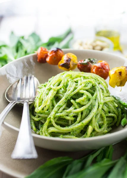 Bir kase dolusu yeşil pesto spagettisi ve hafif bir tabakta ızgara domates.
