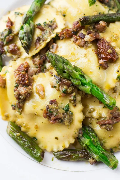 Beyaz bir tabak ravioli, pesto ve kuşkonmaz.
