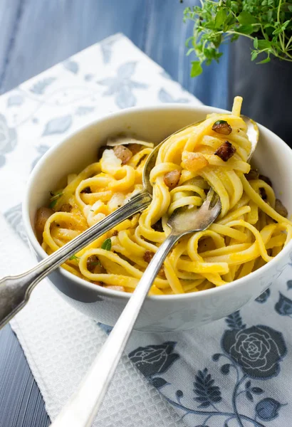 Beyaz kâse spagetti carbonara ve üzerinde mavi gri arka planda parmesan peyniri olan pastırma.