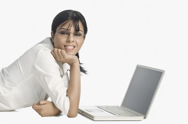 Woman lying in front of a laptop and smiling — Stock Photo, Image