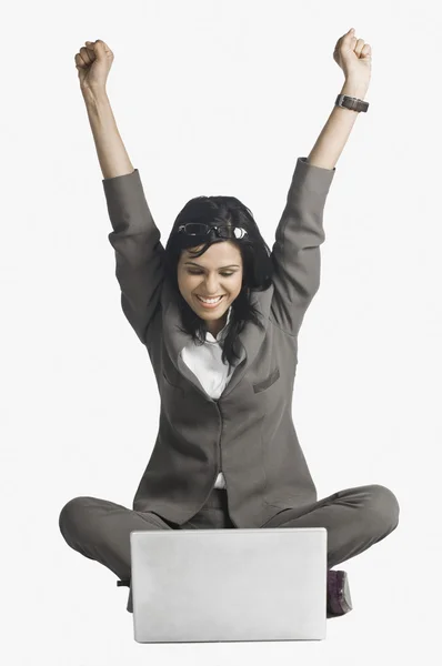 Woman smiling with her arms raised in front of a laptop — Stock Photo, Image