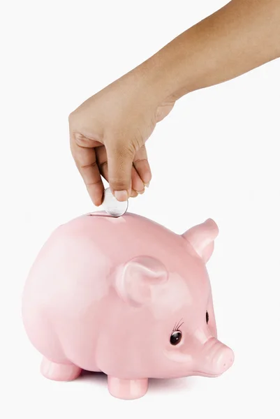 Mão colocando uma moeda em um banco porquinho — Fotografia de Stock