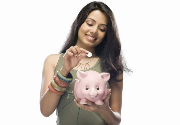 Woman putting a coin into a piggy bank — Stock Photo, Image