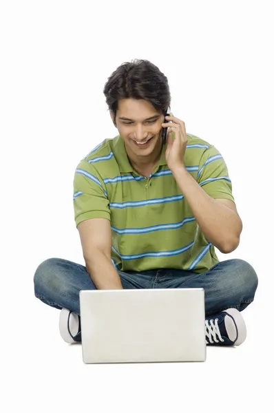 Man met behulp van een laptop en praten op een mobiele telefoon — Stockfoto